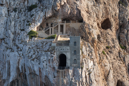 Front view of facade in the middle of the cliff of Porto Flavia, a zinc a mine gallery designed by Engineer Cesare Vecelli in 1924, Masua, on Sardinia island in Italy. Tourist site in Italyの写真素材