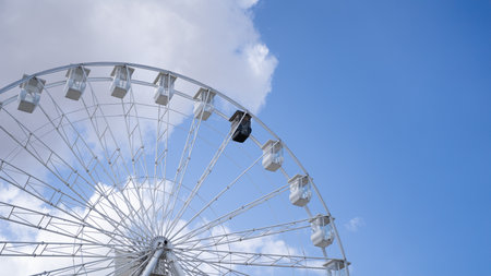 Partial view of a ferris wheel with the white cabins and one black in an amusement park against a clear blue sky. Amusement park conceptの写真素材