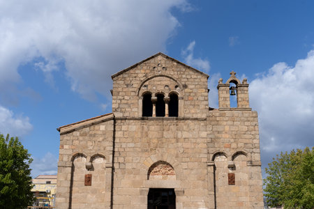 The front view of the Basilica of San Simplicio, a historic Romanesque church located in Olbia, Sardinia, Italy. Stonework ancient facade, arched windows, and a bell tower under a blue sky. Tourist spot in Olbiaの写真素材