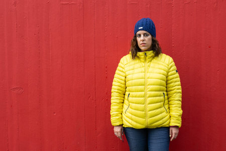 Portrait of a brunette Caucasian woman in her 30s looking at camera serious, wearing a yellow anorak...