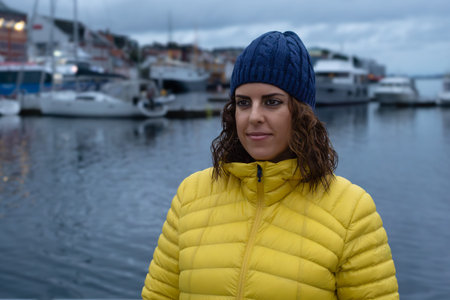 Portrait of a brunette woman in her 30's wearing a yellow padded jacket and a blue woolen hat...
