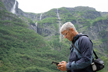 A gray haired man in his 40's with a focused expression holds a remote control drone, standing with...