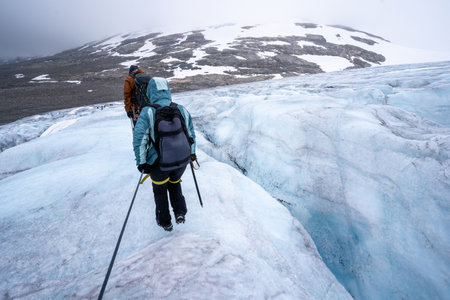 Two people are walking near a large crevasse on the Austdalsbreen Glacier in Jostedal, Norway. They are roped together and equipped with necessary gear, view from behind. Extreme sport conceptの写真素材