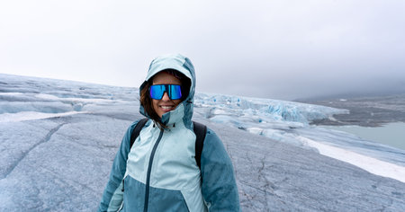 Portrait of a brunette woman in her 30s, looking at camera smiling, dressed in mountaineering gear, stands on the unspoiled icy expanse of Austdalsbreen Glacier in Jostedal, Norway. Extreme sport conceptの写真素材