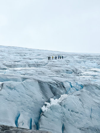 Group of unrecognizable hikers chained together on a rope walking across the Austdalsbreen glacier...
