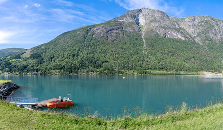 View of Innvikfjorden fjord with a little pier with an orange motorboat moored in a summer day and...