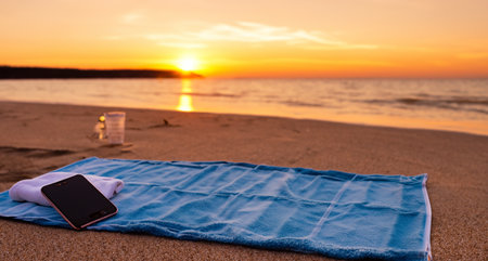 a towel and a cell phone on a beach at sunsetの写真素材