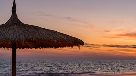 an umbrella and a bed on a beach at sunsetの写真素材