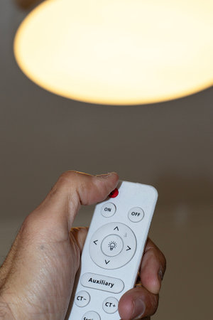 a man's hand holding a remote control of a lampの写真素材