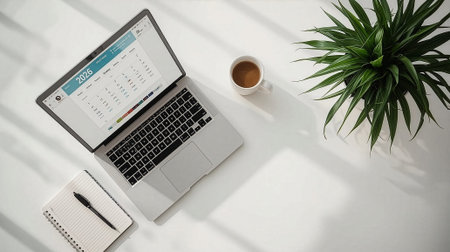 Top view of a modern workspace with a laptop displaying a 2026 calendar, a notebook, and a cup of...