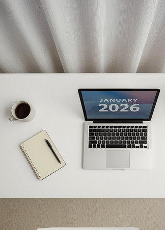 A modern computer on a white desk displaying January 2026 on the screen, accompanied by a coffee cup and a notebook.の写真素材