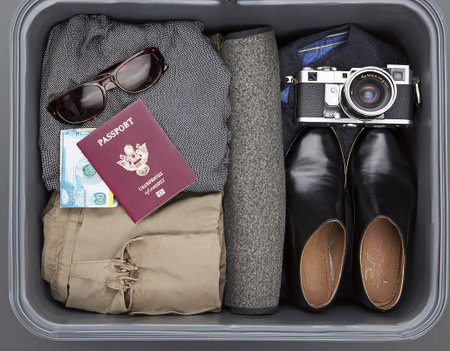 A neatly organized suitcase displays essential travel items, including clothing, sunglasses, a passport, cash, and a vintage camera ready for an international journey.の写真素材
