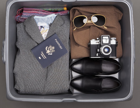 A neatly organized suitcase displays essential travel items, including clothing, sunglasses, a passport, cash, and a vintage camera ready for an international journey.の写真素材