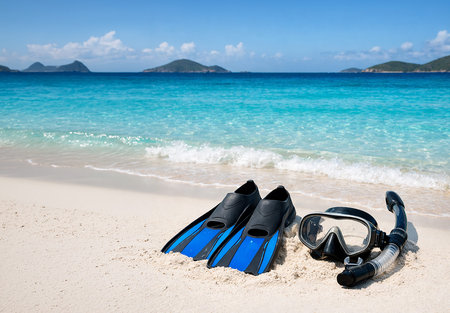 A pair of blue and black swim fins and a professional diving mask with a snorkel are placed on a pristine white sand beach.の写真素材