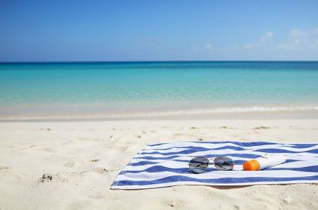 A bright orange sunscreen bottle and stylish black sunglasses are neatly placed on a blue and white...