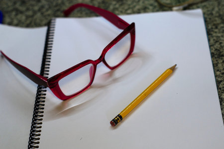 Red Eyeglasses and Yellow Pencil on Blank Spiral Notebook Page
