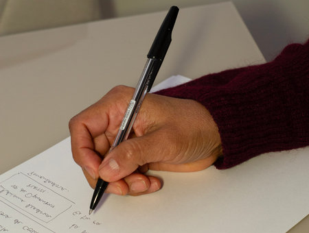 A detailed close-up shot focusing on a person's hand holding a black ballpoint pen, actively writing...