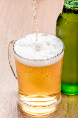 Beer pouring from top in bottle on wood tableの写真素材