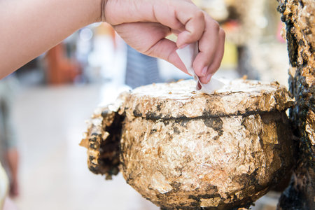 human hand sticking golden leaves on Buddhist monk's bowl
