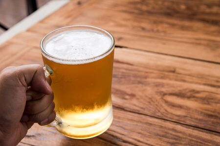 hand holding beer in mug glass on wood tableの写真素材