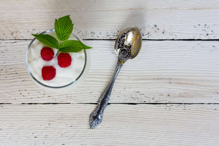 yogurt with berries of raspberry and a spoon on a white wooden tableの写真素材