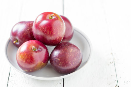 big ripe plums in a ceramic saucer on white boards closeup