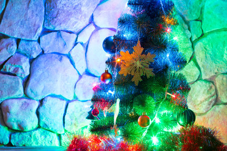Christmas lights and colorful toys on New Year tree on a background of a stone wall in the eveningの写真素材