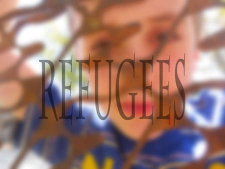 inscription refugees in the blurred image of a boy looking through a rusty metal fenceの写真素材