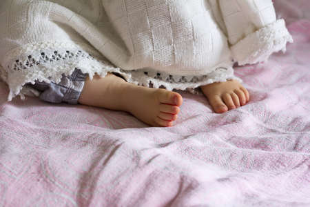 Heel sleeping baby girl sticking out from under the blanket, selective focusの写真素材