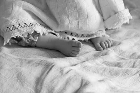 Heel sleeping baby girl sticking out from under the blanket in black and white, selective focusの写真素材