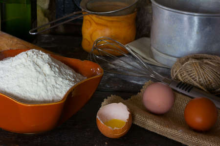 White wheat flour in ceramic ware, broken egg with the yolk, whole eggs and cooking utensils for cooking test. Rustic style. Side view close-up.の写真素材