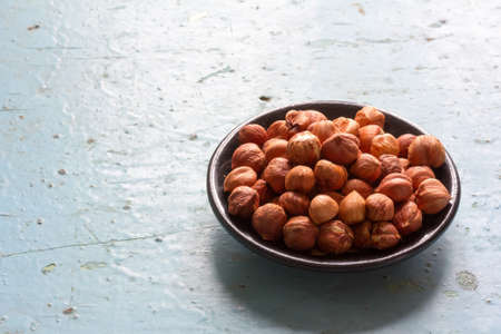 Round black wooden plate with nuts hazelnuts on old blue table closeup. Free space for text. Copy spaceの写真素材