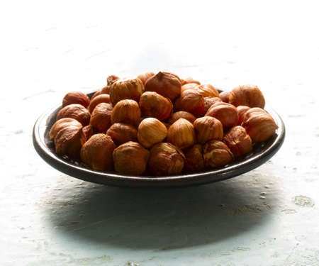 Round black wooden plate with nuts hazelnuts on old blue table closeup. Free space for text. Copy spaceの写真素材