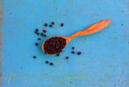 Dried hawthorn fruit in a wooden spoon on blue wooden background. Natural berry beverage production