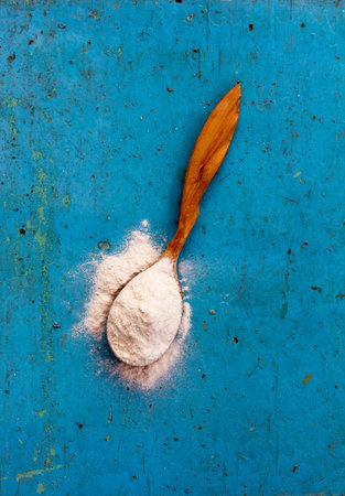 Wooden spoon from the juniper filled with wheat flour on a old bright blue background.