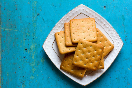 Cracker biscuits in a white ceramic square saucer on old blue background close-up. Free space for...