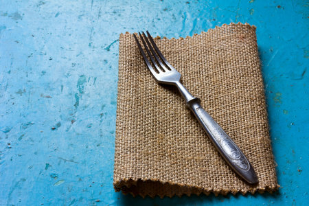 Old vintage fork on a linen napkin on blue background.Free space for text. Copy space. Top view