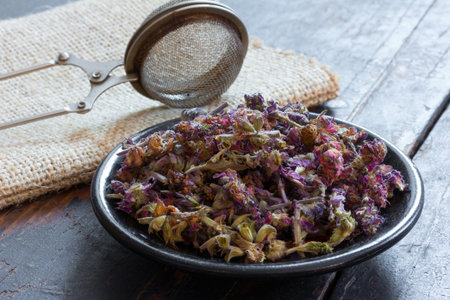 Salvia for making herbal tea on a black saucer and a strainer for brewing tea on the matting on the...