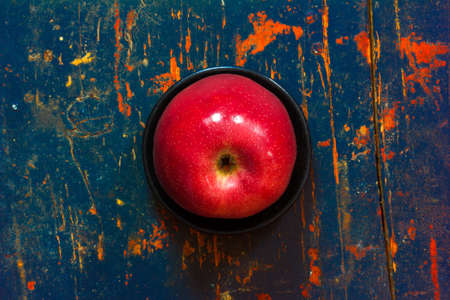 Red ripe apple in a black saucer on old cracked board with spots. Closeup, top viewの写真素材