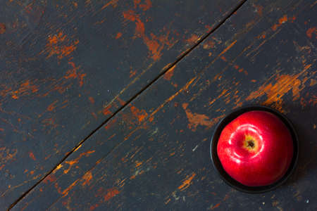 Red ripe apple in a black saucer on old cracked board with spots in the lower right corner. Copy space. Free space for text, Close-up, top viewの写真素材