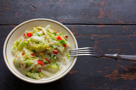 Vegetable salad made of fresh cabbage, radish, cucumber, bell pepper and sour cream in a white plate and fork stainless steel on the old black table. Top view closeup, selective focusの写真素材