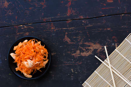 Korean salad made of grated carrots with red onions and fish sauce and chopsticks on the old black cracked background, Close-up, top viewの写真素材