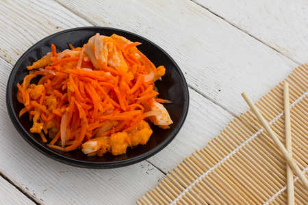 Korean salad made of grated carrots with red fish and onions marinated in a black plate and wooden chopsticks on white wooden boards. Close-up, top viewの写真素材