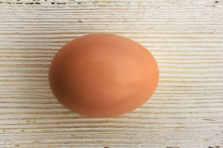 Brown chicken egg in shell on a white wooden background. Shallow depth of field. Top view closeup