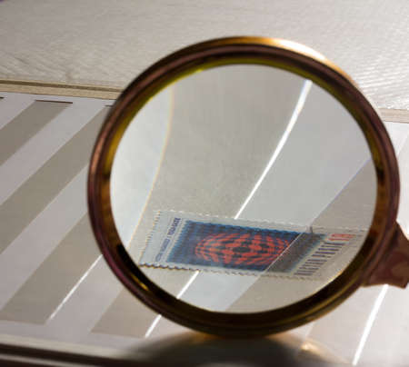 Look for the stamp in the white stamp-album through a magnifying glass. The concept of philately and collecting, selective focusの写真素材