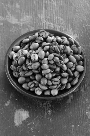 Roasted coffee beans in a round black saucer on old wooden background closeup. black and white photoの写真素材