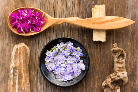 purple flower petals plants dead-nettle in a wooden spoon and pale blue flowers Persian speedwell on an old wooden board in the cracks close up. view from above. aromatherapy, herbal tea, homeopathic medicineの写真素材