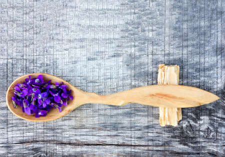Petals forest violets in a wooden spoon on old gray wooden board in the cracks close up with space for textの写真素材
