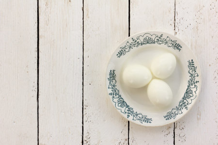 boiled chicken eggs without the shell on a ceramic saucer on a white wooden background. with space...