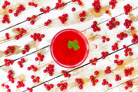 freshly squeezed red juice with green leaf currant and bunches of redcurrants on a white wooden...